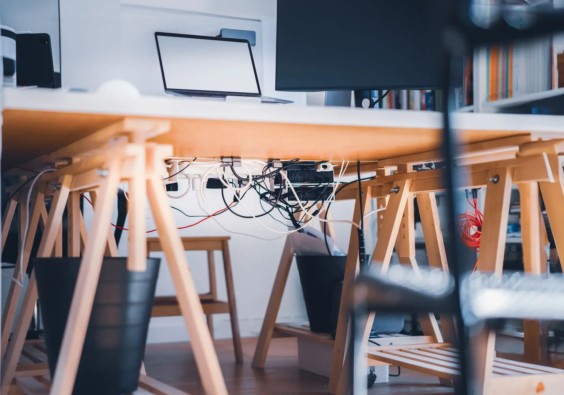 A tangle of cables and a power strip under a trestle desk, the clutter a living room office combo needs to hide