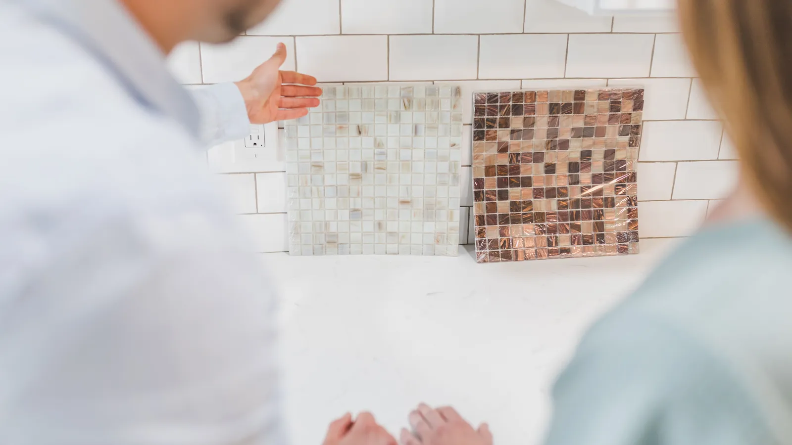 Tile sheets held up against a white subway tile backsplash near an outlet to check the layout before installing