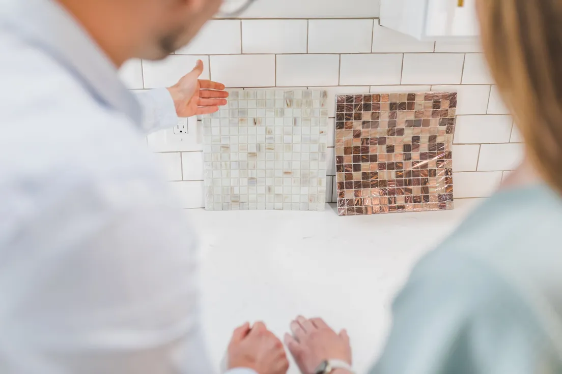 Tile sheets held up against a white subway tile backsplash near an outlet to check the layout before installing