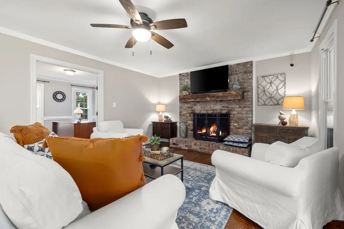 A budget modern farmhouse living room with white slipcovered seating, a brick fireplace, rustic wood mantel, and a blue vintage-style rug