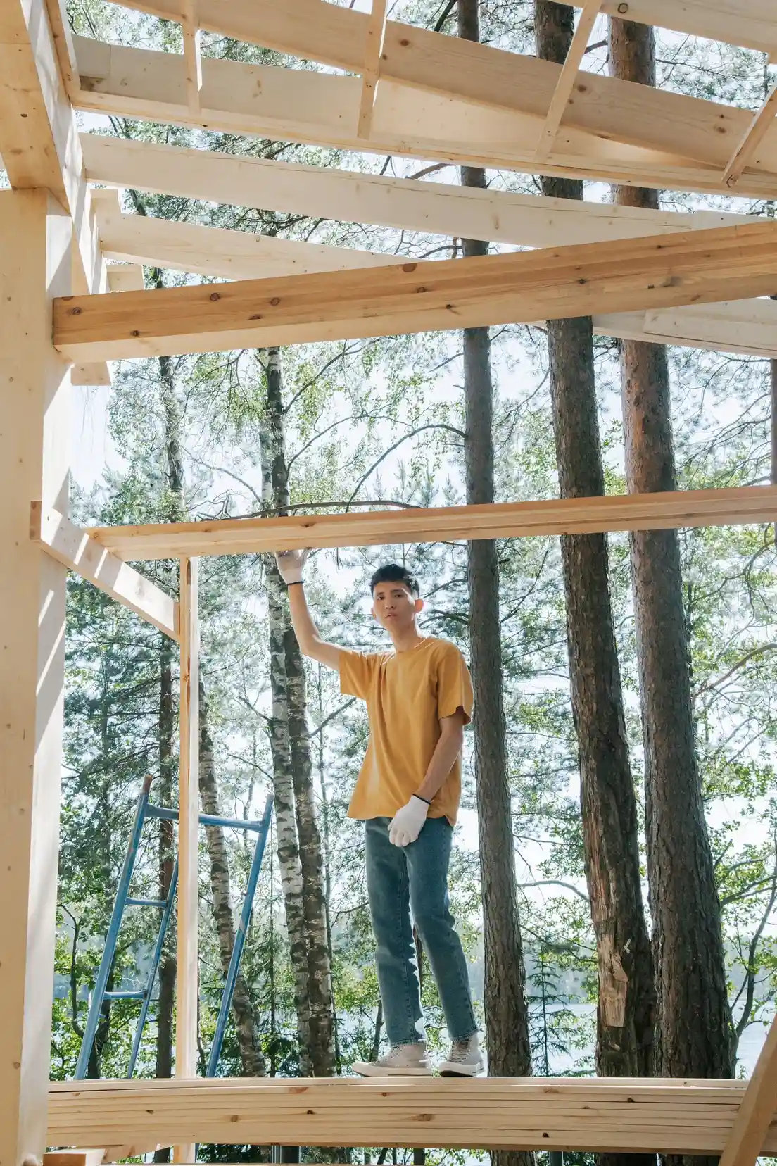 A person building a wood patio cover frame themselves in a backyard