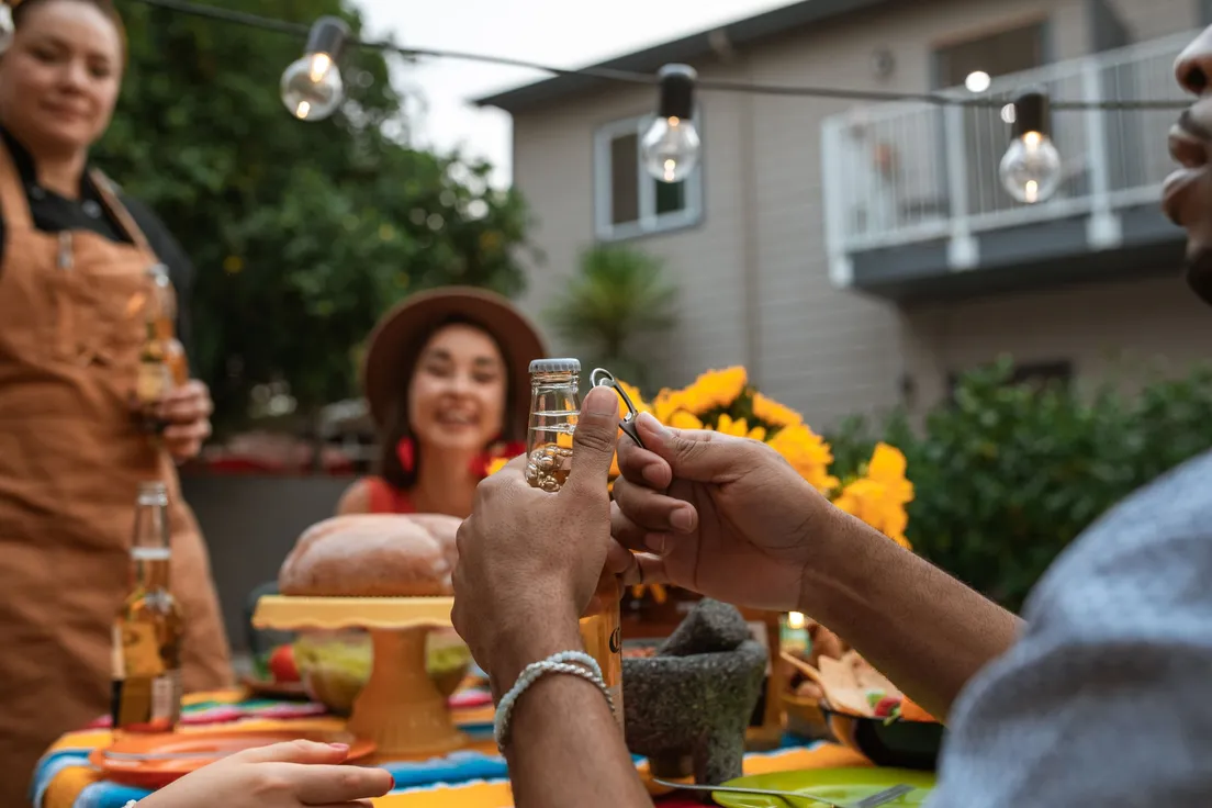 Friends gathered around a backyard party table with string lights and drinks