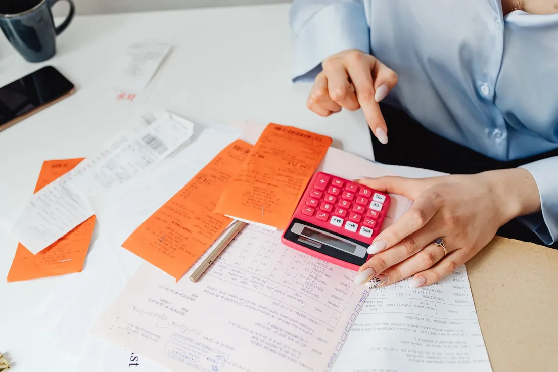 A person adding up a modern farmhouse exterior project budget with receipts and a calculator