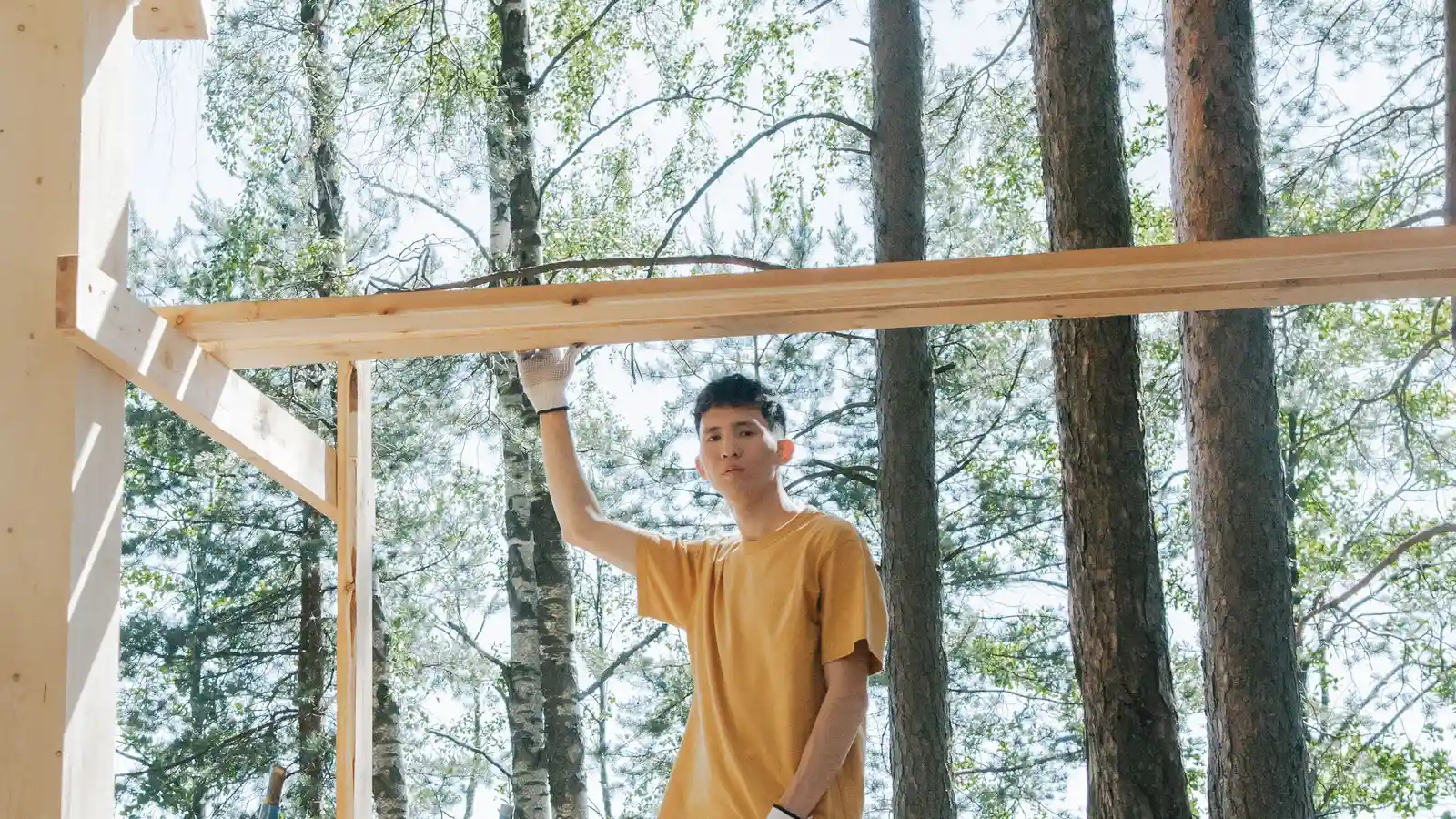 A person building a wood patio cover frame themselves in a backyard