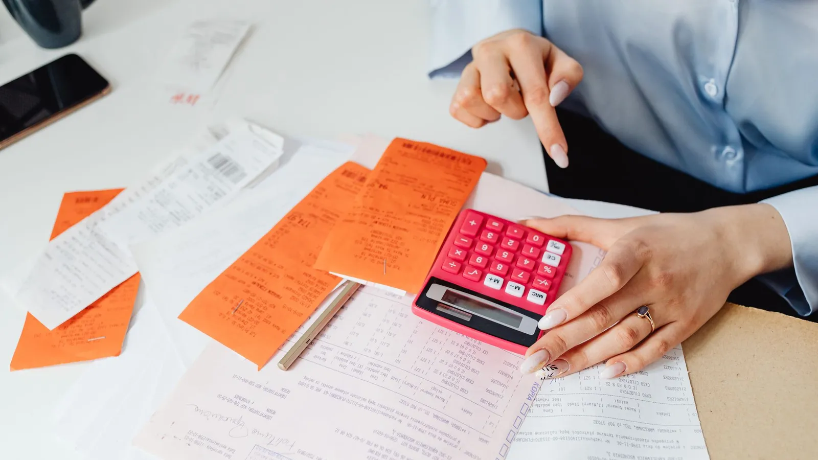 A person using a pink calculator to add up receipts on a desk