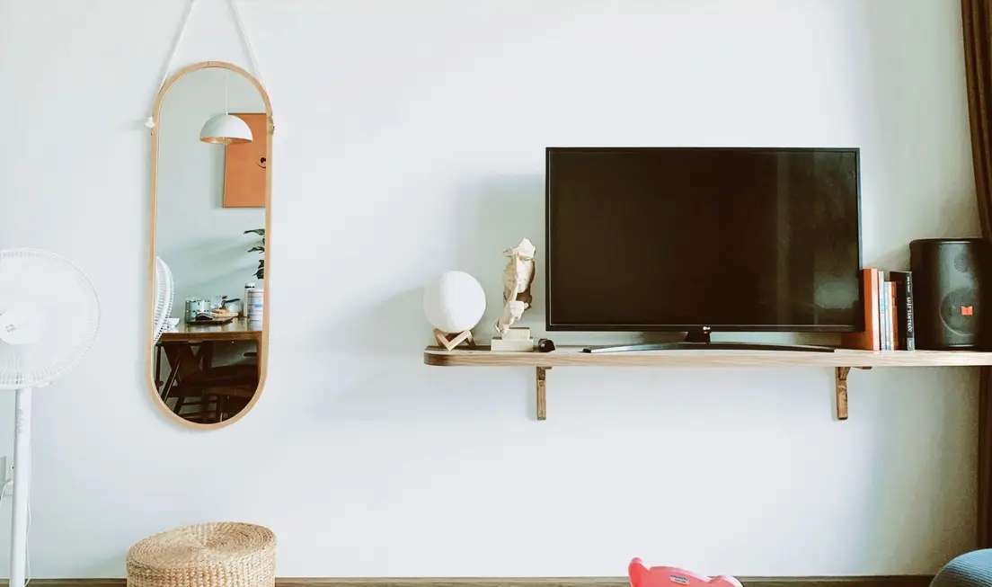 A TV on a floating wood shelf mounted against a plain wall