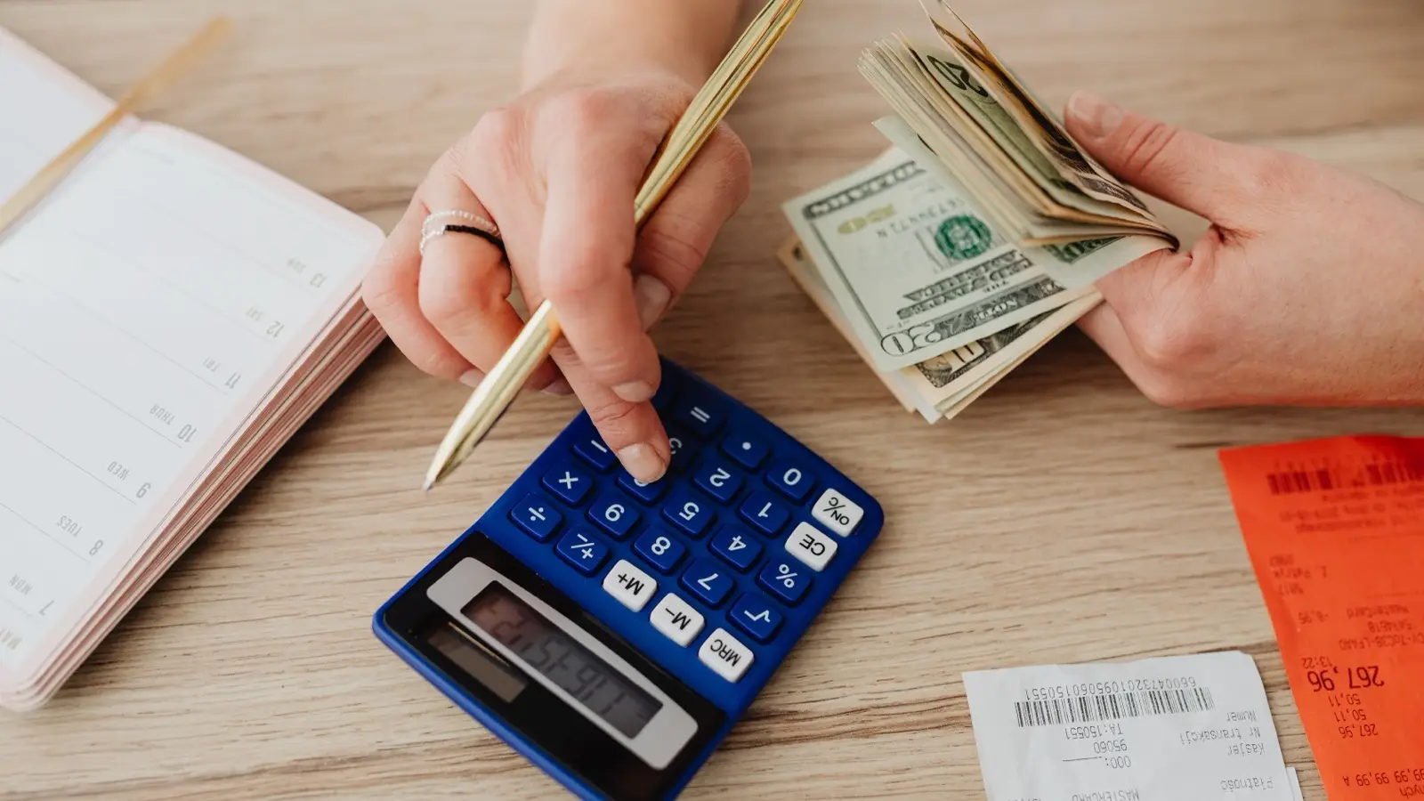 Hands counting cash and using a calculator with receipts to add up a home decor budget