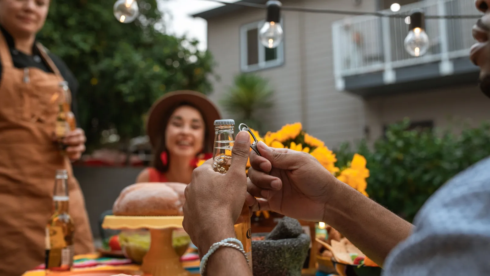 Friends gathered around a backyard party table with string lights and drinks