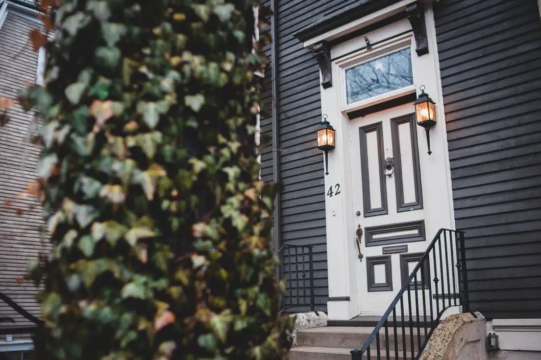 A white front door with matching black lantern sconces and painted house numbers on dark gray siding