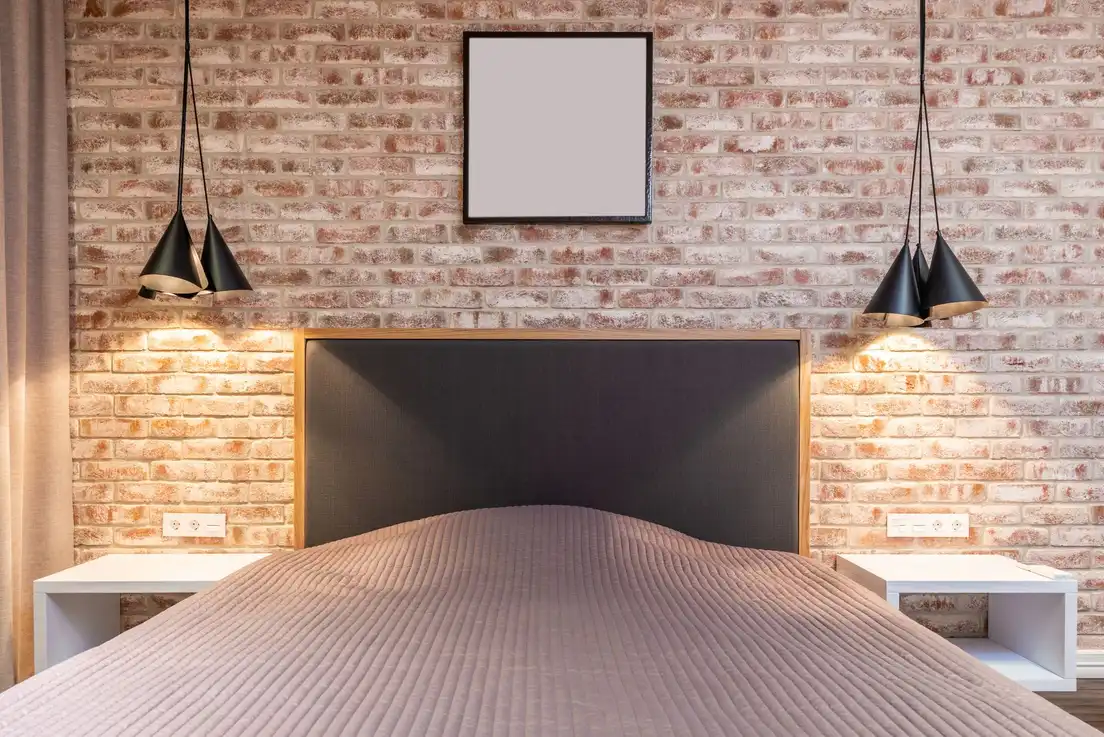 An industrial-style bedroom with an exposed brick wall, black pendant lights, and a dark headboard