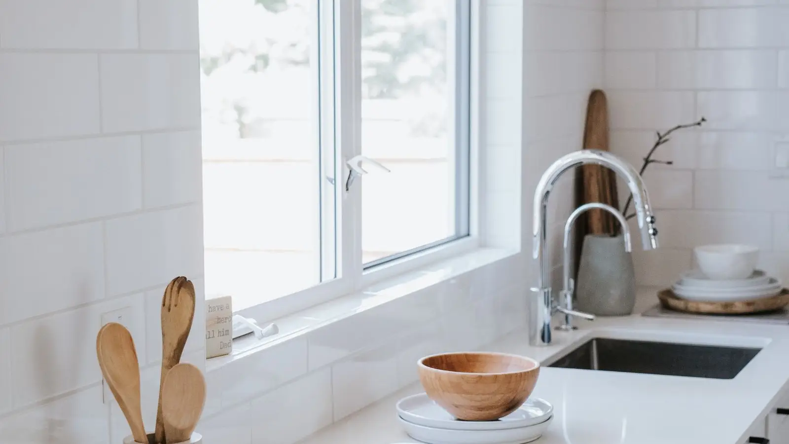 A white subway-tile japandi kitchen counter with a wooden bowl, cutting board, and utensil jar