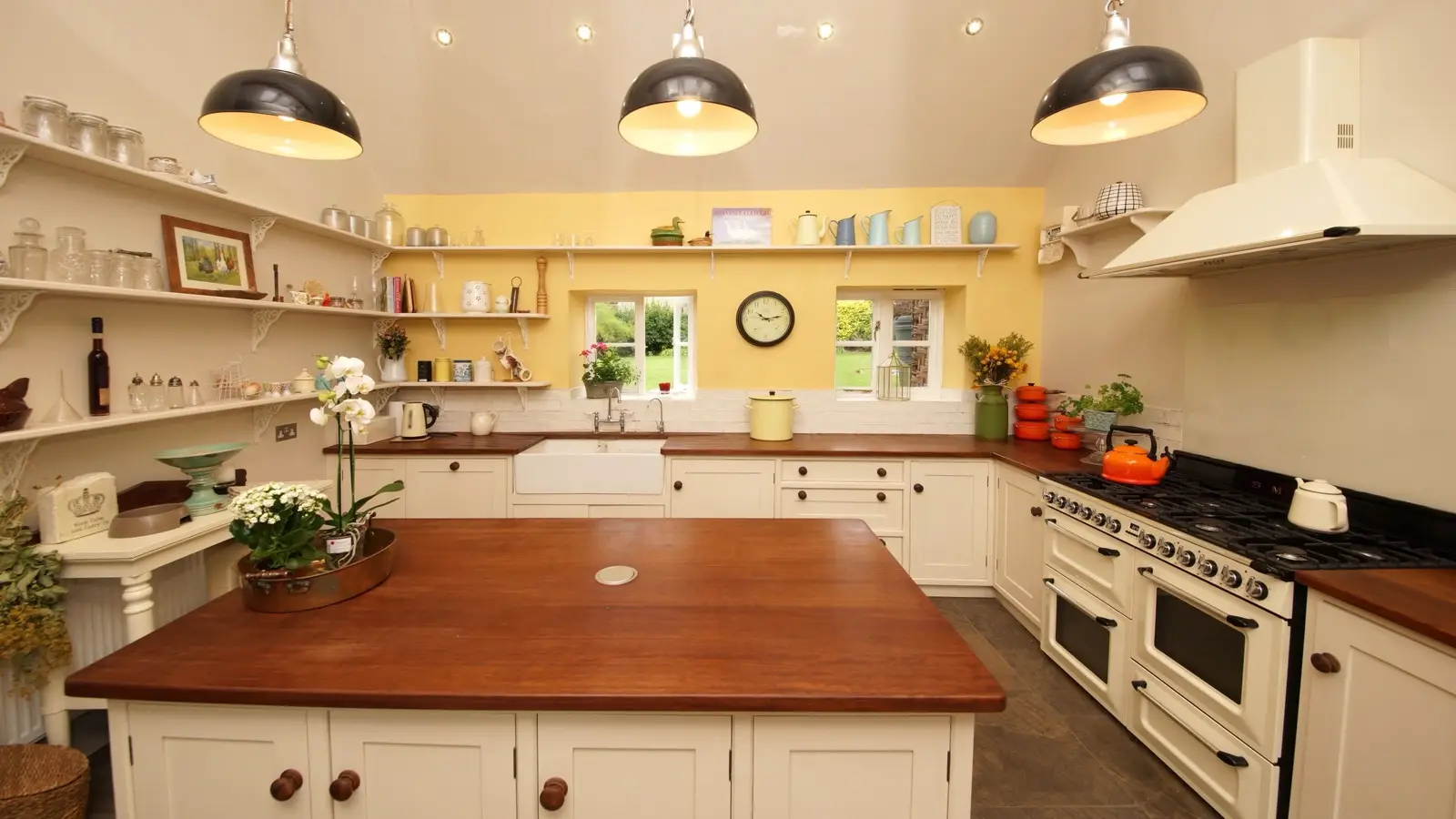 A modern farmhouse kitchen with black pendant lights, open shelving, and a butcher block island