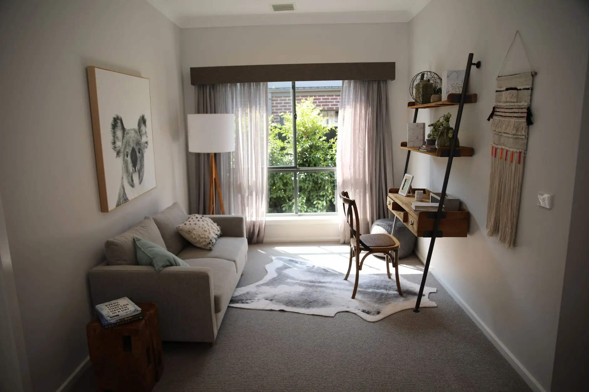 A leaning ladder wall desk with wood shelves in a living room beside a gray sofa and cowhide rug