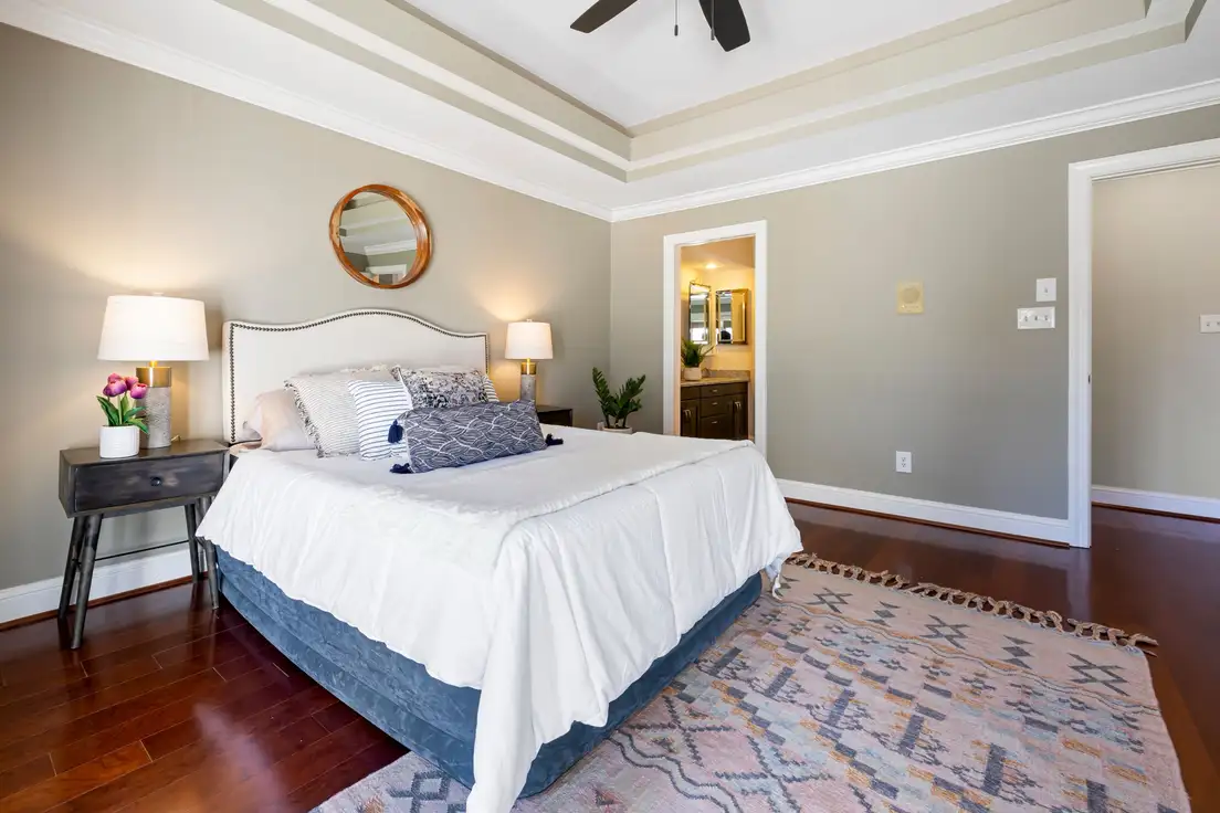 A bed with an upholstered headboard and a large patterned area rug extending out on both sides onto a hardwood floor