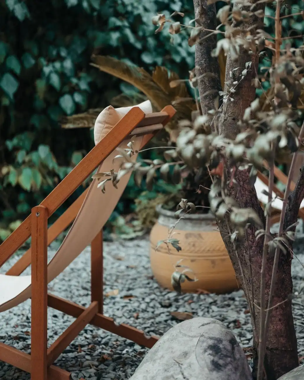 A pea gravel patio surface with a wooden deck chair and a potted plant