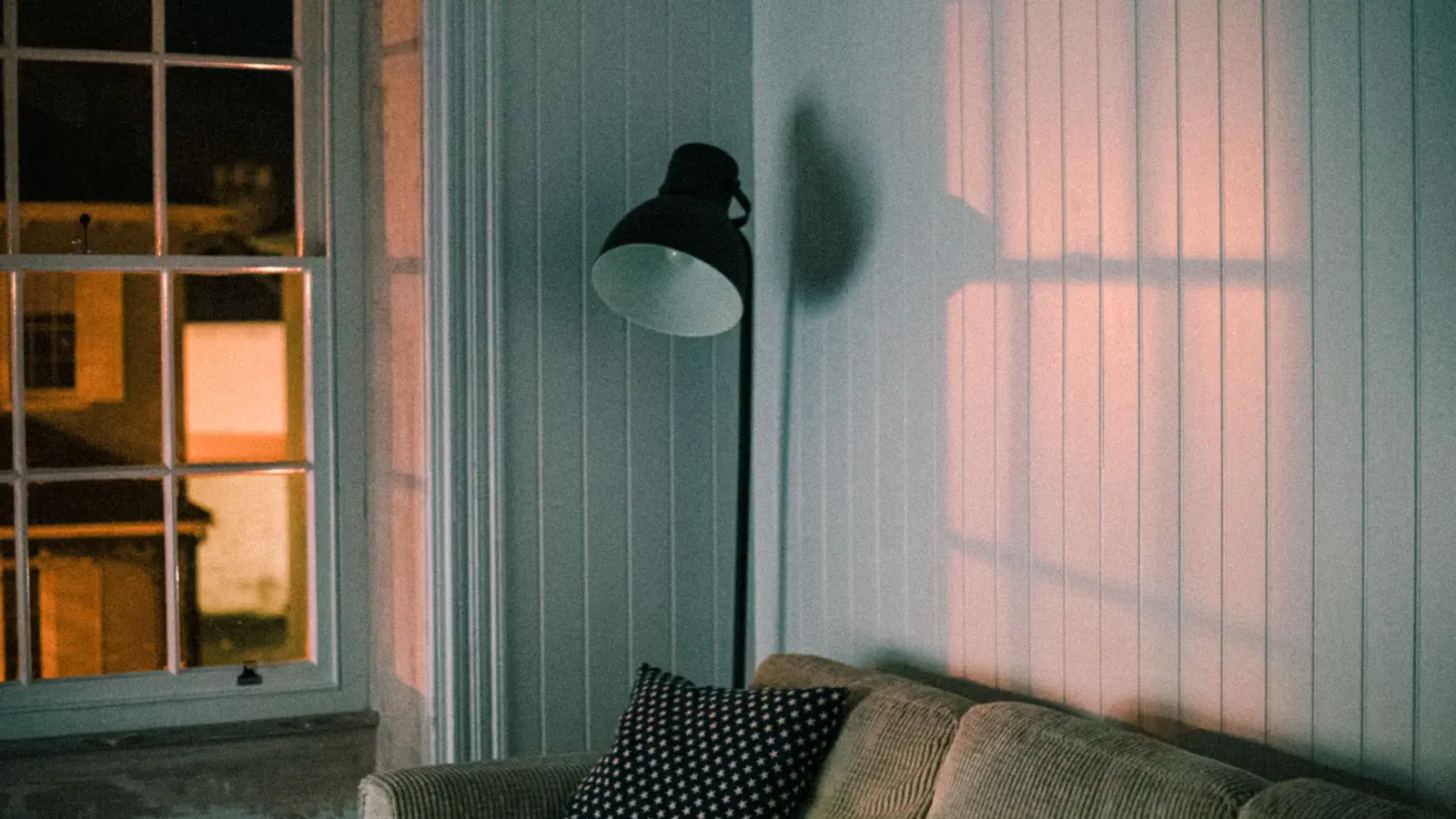 A black floor lamp beside a couch, layering warm lighting in a small apartment living room