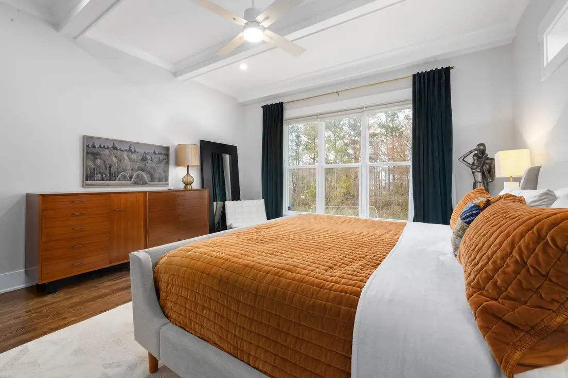A small master bedroom with a bed centered between two windows and a dresser opposite