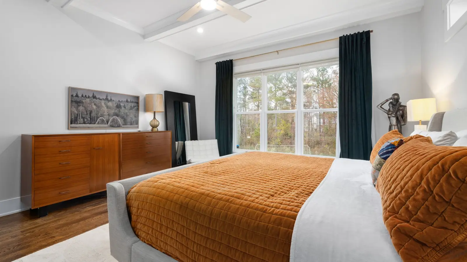 A small master bedroom with a bed centered between two windows and a dresser opposite