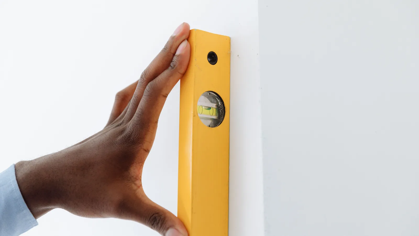 A hand holding a yellow level against a plain wall to mark a straight starting line for tile