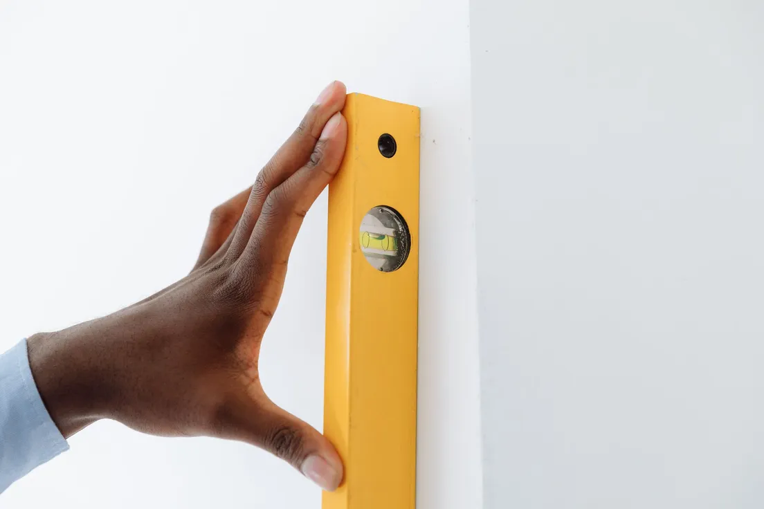 A hand holding a yellow level against a plain wall to mark a straight starting line for tile