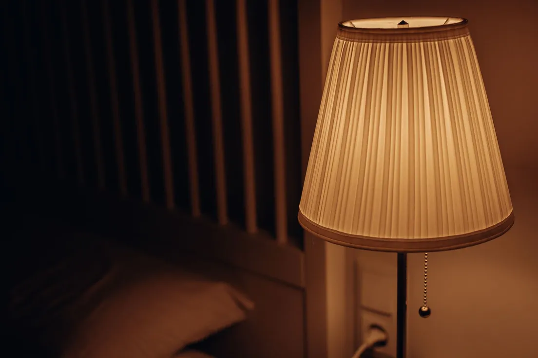 A warm ceramic table lamp glowing softly beside a bed