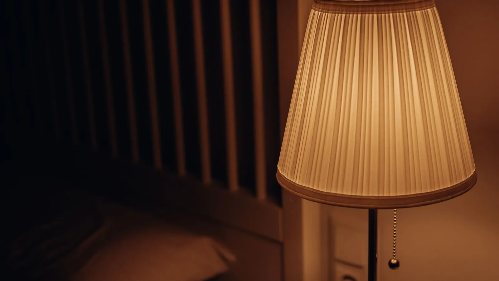 A warm ceramic table lamp glowing softly beside a bed