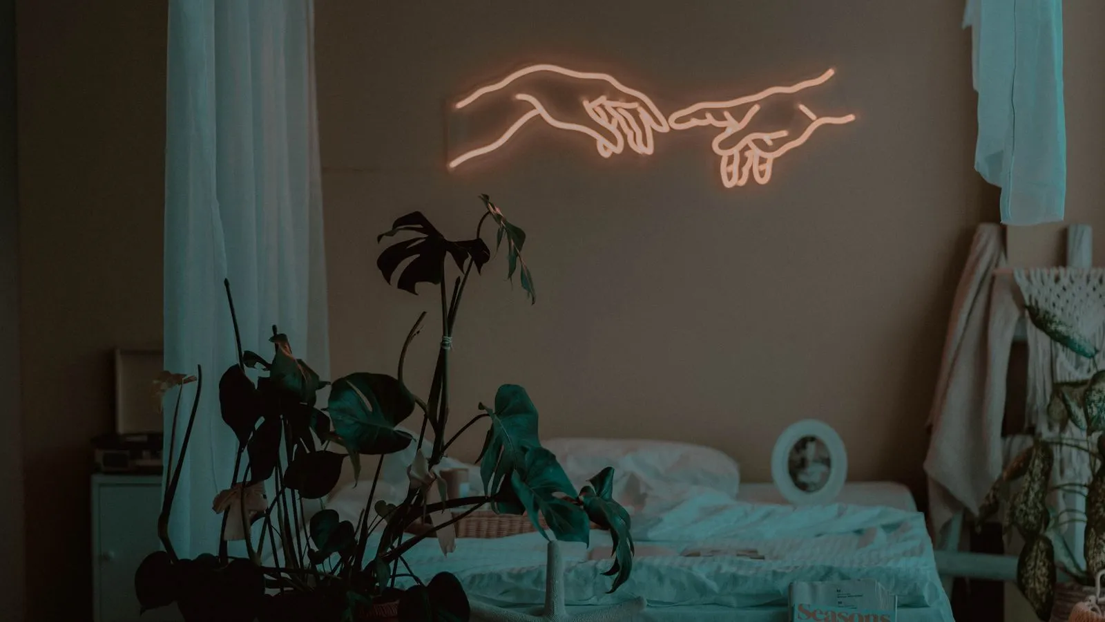 A dim bedroom lit by a warm coral neon sign shaped like hands above the bed