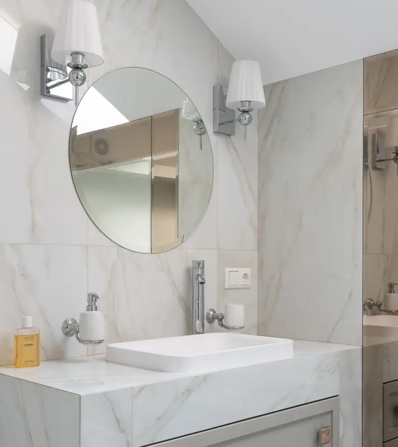Marble bathroom wall with a pair of sconces flanking a round mirror over a vessel sink