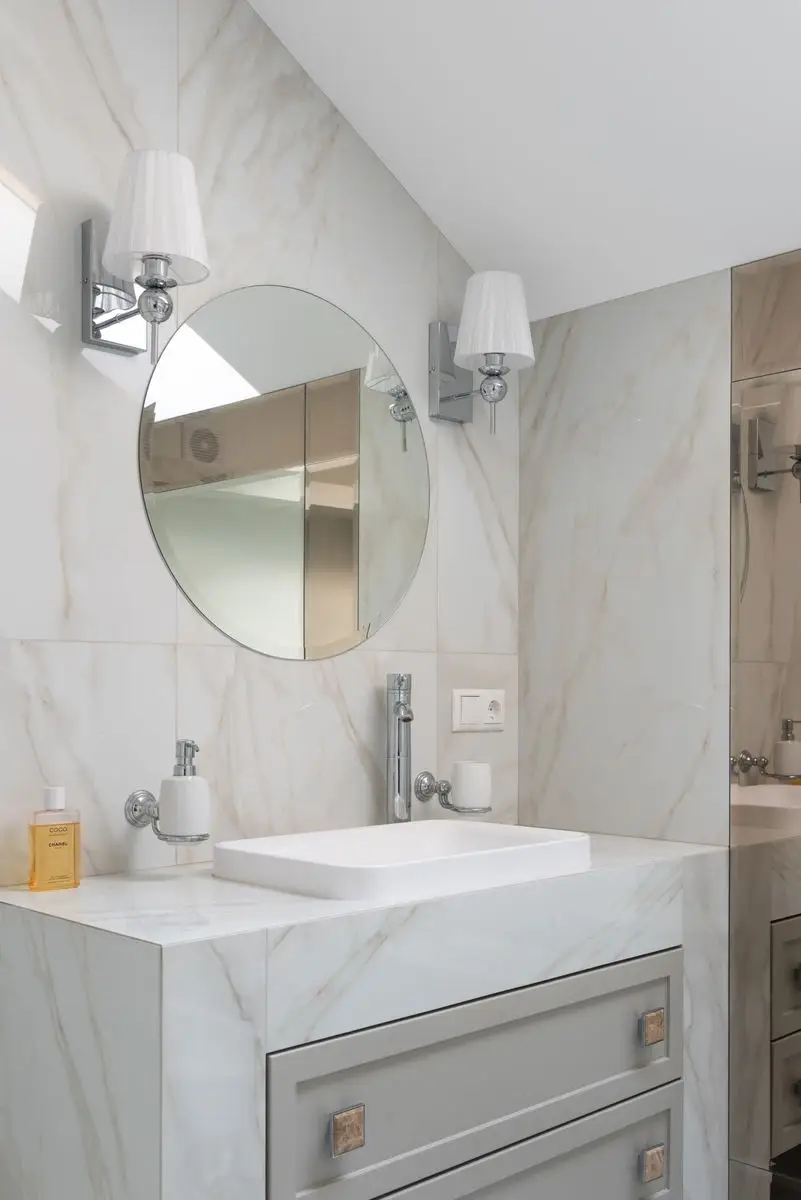 Marble bathroom wall with a pair of sconces flanking a round mirror over a vessel sink