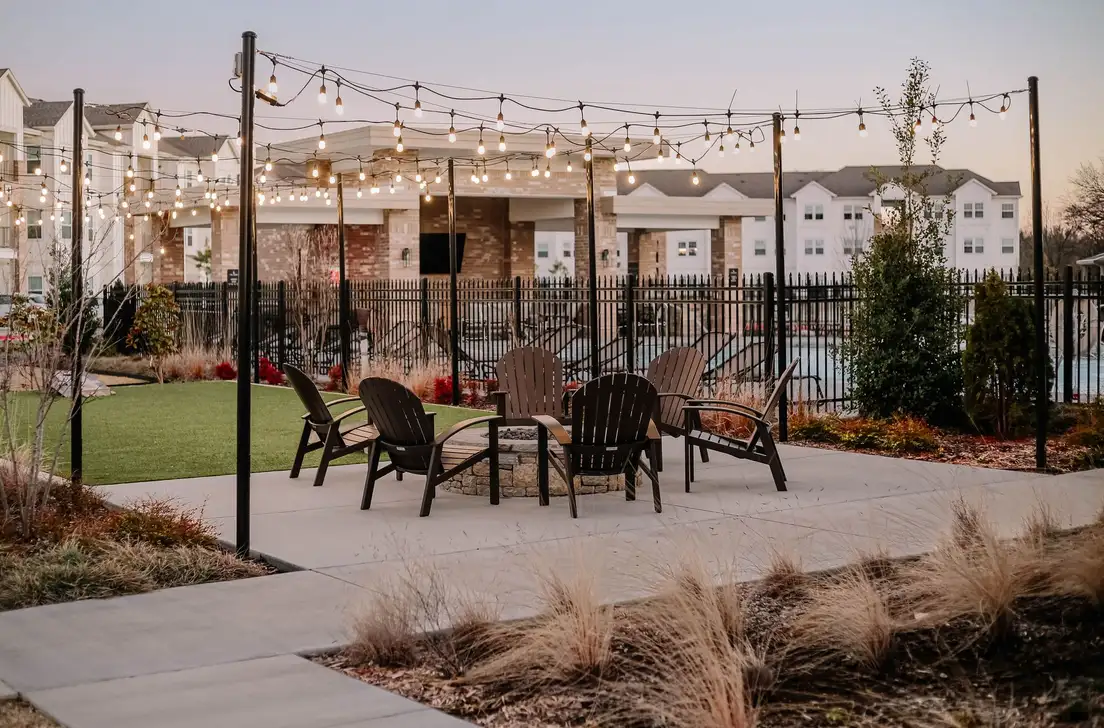 String lights over an outdoor patio seating area near a backyard bbq zone at dusk