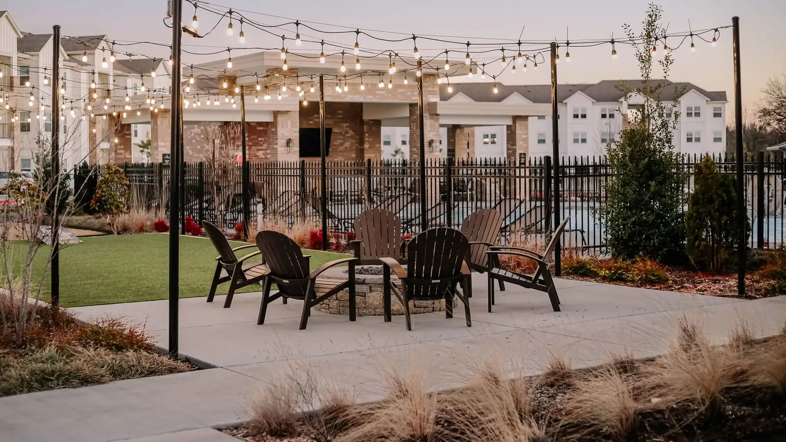 String lights over an outdoor patio seating area near a backyard bbq zone at dusk