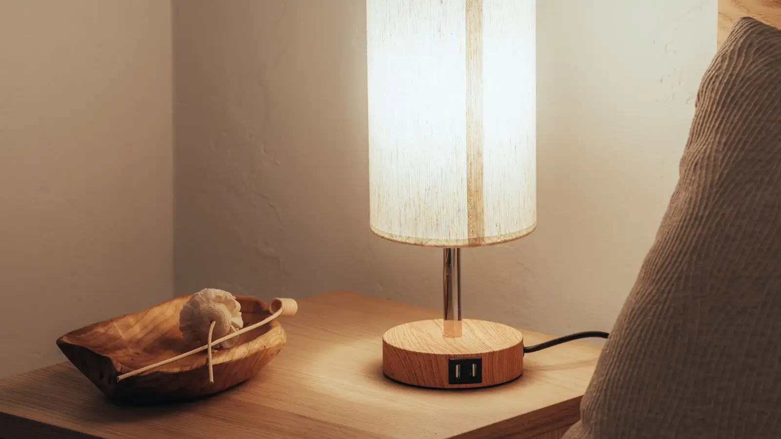 A warm wood table lamp glowing on a bedroom nightstand at night