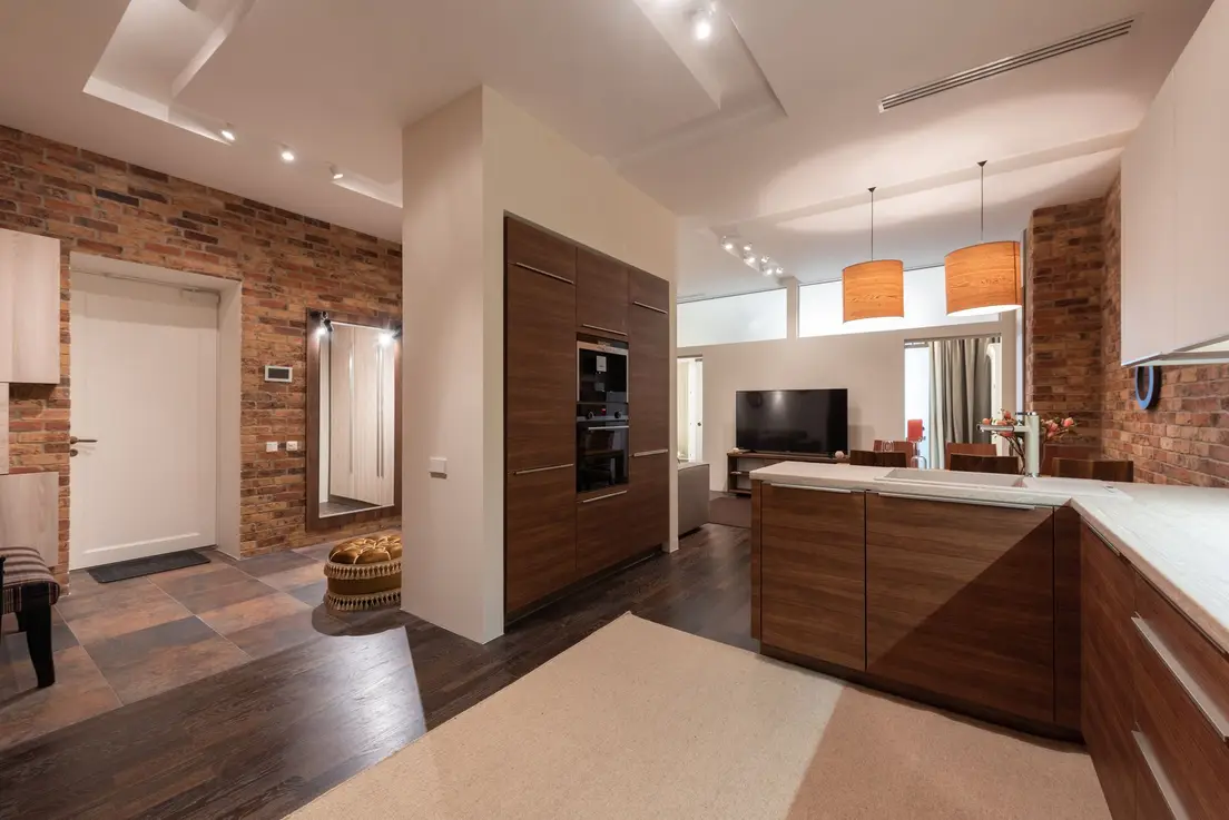 A pendant light fixture over a kitchen counter beside a warmly lit small living room seating area