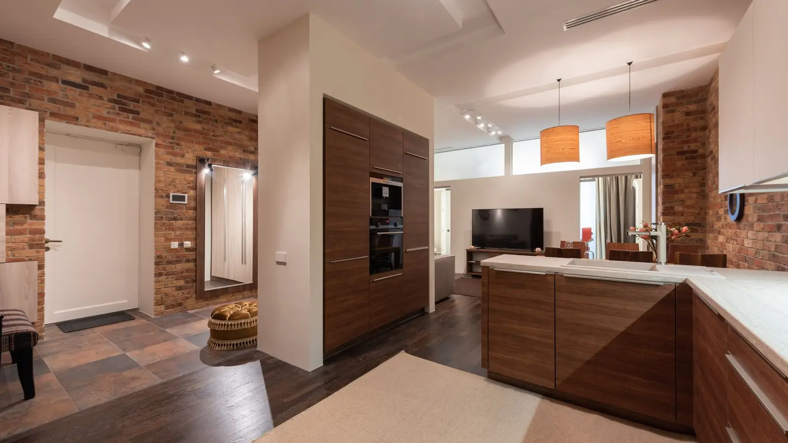 A pendant light fixture over a kitchen counter beside a warmly lit small living room seating area