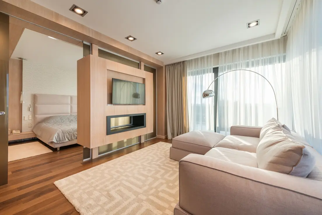 A warm arc floor lamp beside a sectional sofa in a minimalist living room at golden hour