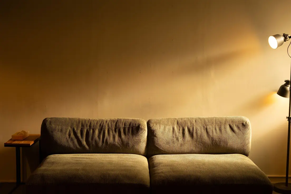 A warm floor lamp casting golden light on a corduroy sofa in a dim living room