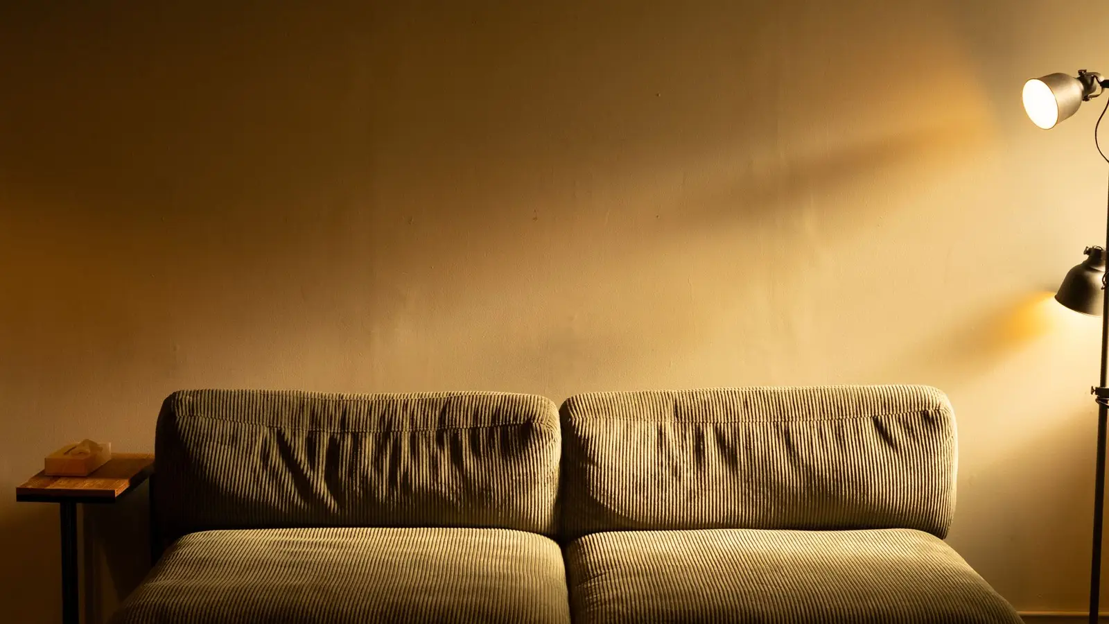 A warm floor lamp casting golden light on a corduroy sofa in a dim living room