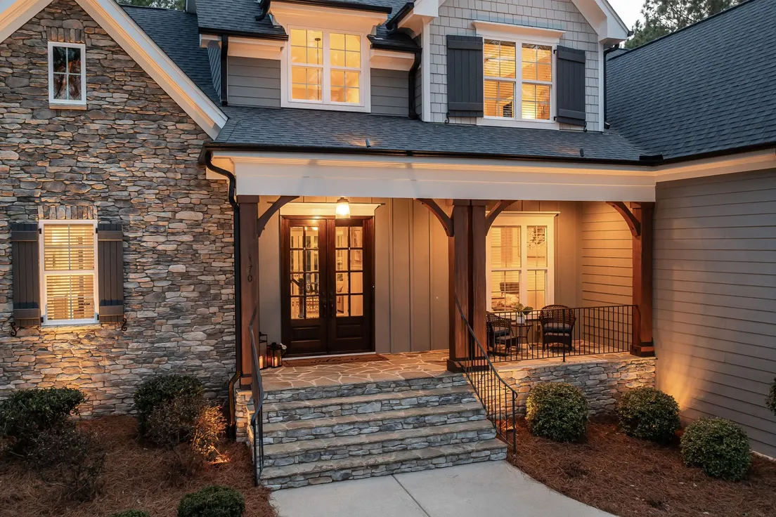 A stone-facade house exterior lit with warm porch and landscape lighting at dusk