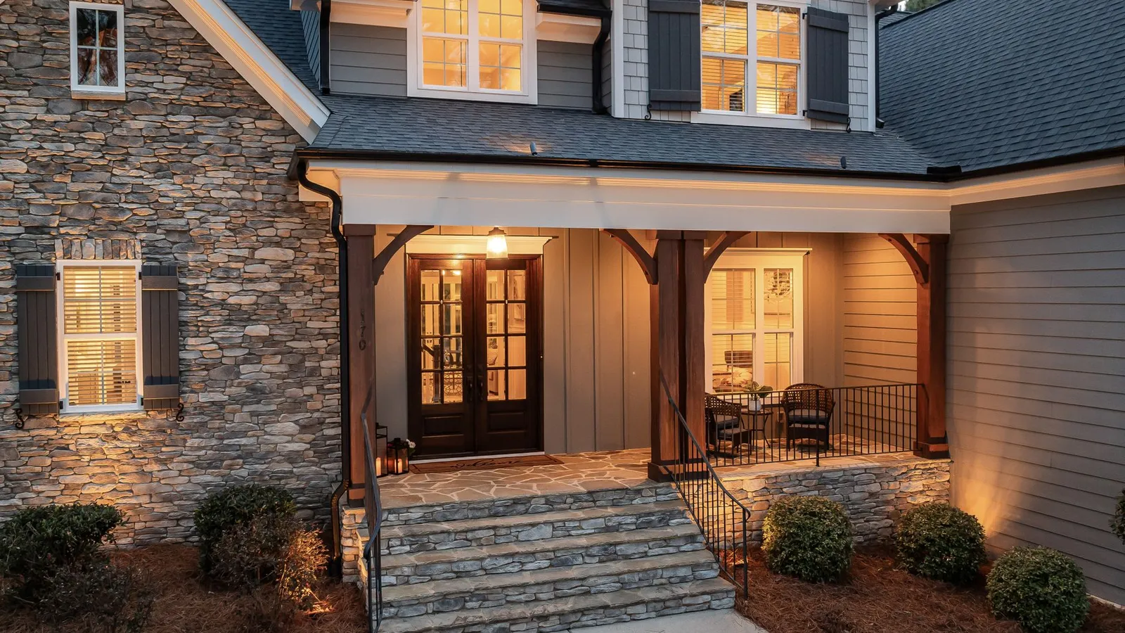 A stone-facade house exterior lit with warm porch and landscape lighting at dusk