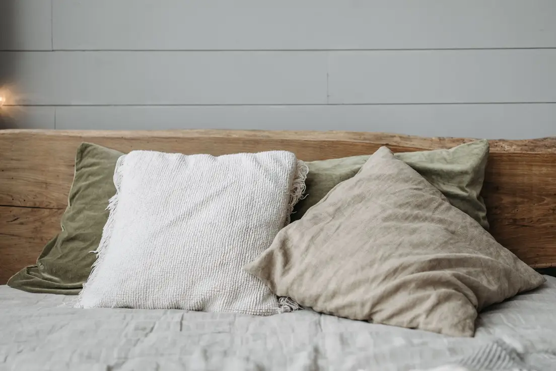 An organic modern bedroom with a live-edge wood headboard and linen pillows in cream and sage green