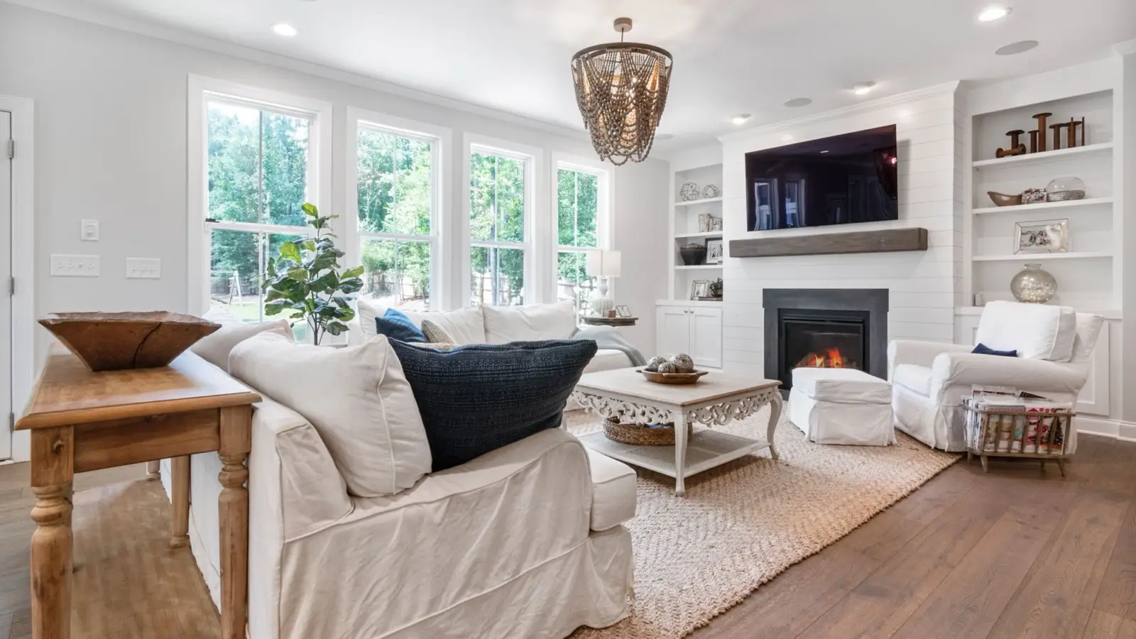 A modern farmhouse living room with a white shiplap fireplace, built-in shelving, and a slipcovered sofa on a jute rug