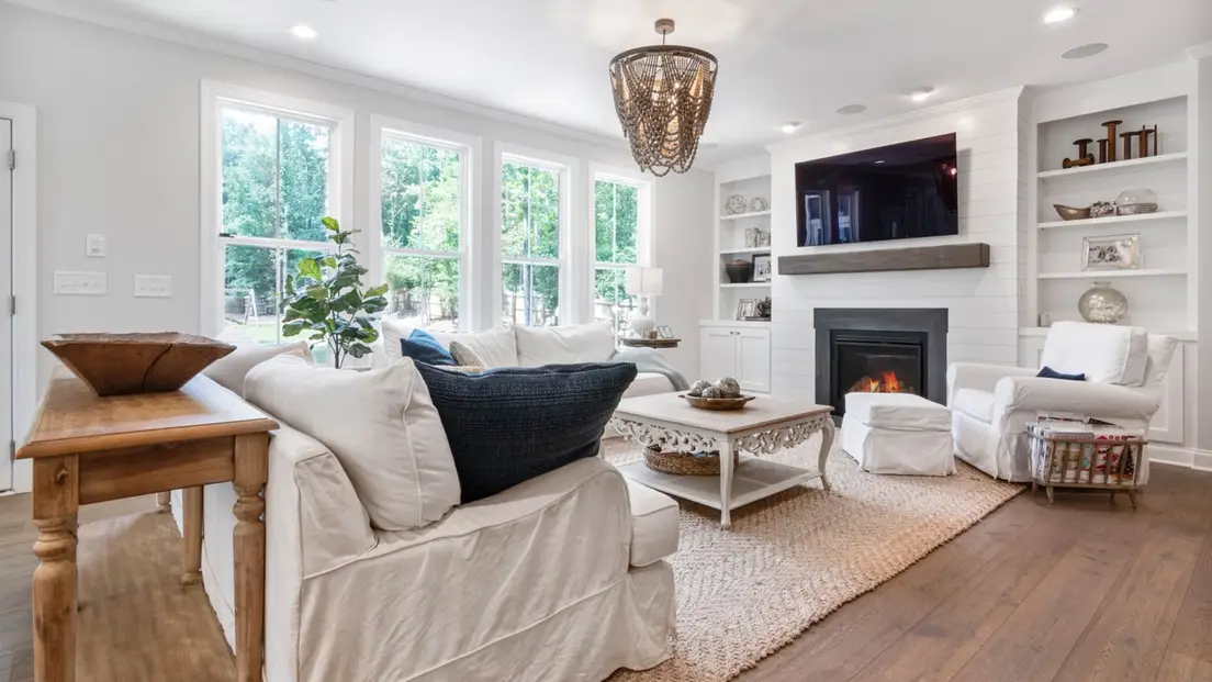 A modern farmhouse living room with a white shiplap fireplace, built-in shelving, and a slipcovered sofa on a jute rug