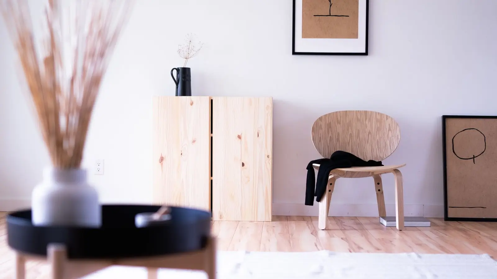 A bright, uncluttered japandi living room corner with a pine cabinet, wood chair, and framed line art