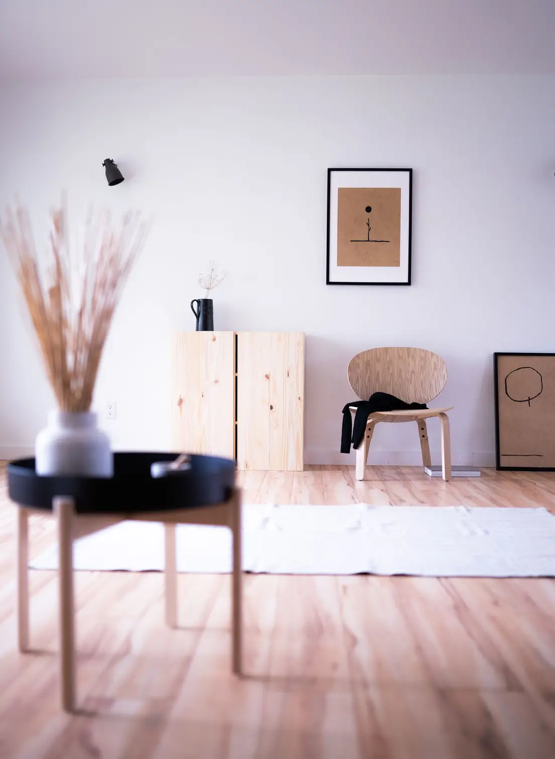 A bright, uncluttered japandi living room corner with a pine cabinet, wood chair, and framed line art