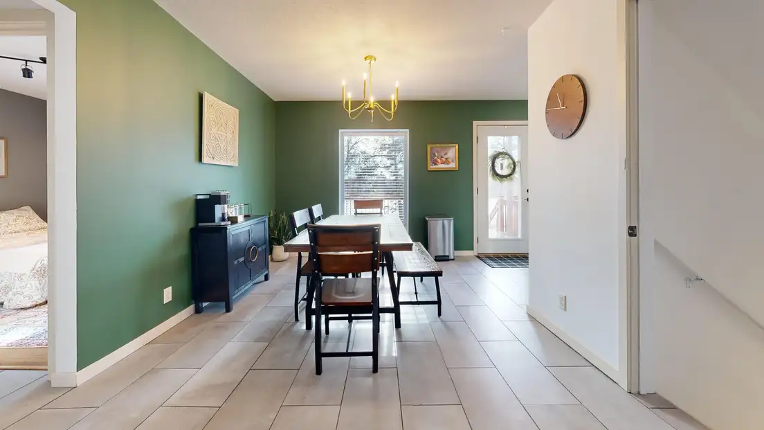 A long narrow dining area with a wood table, bench, and sideboard along a green wall, with the walkway kept along one side of the rectangular room