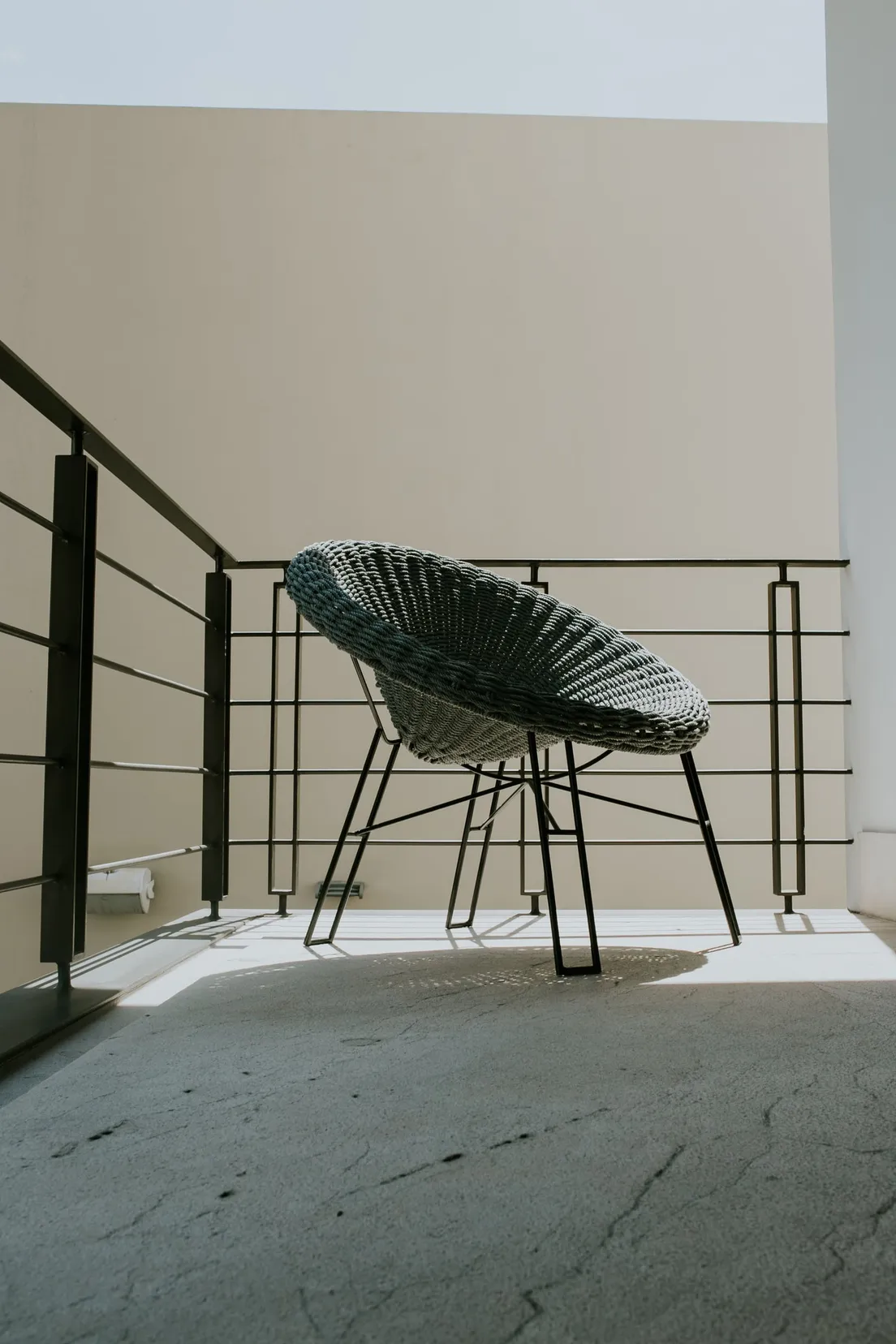 A woven scoop lounge chair on a minimalist apartment balcony in afternoon light