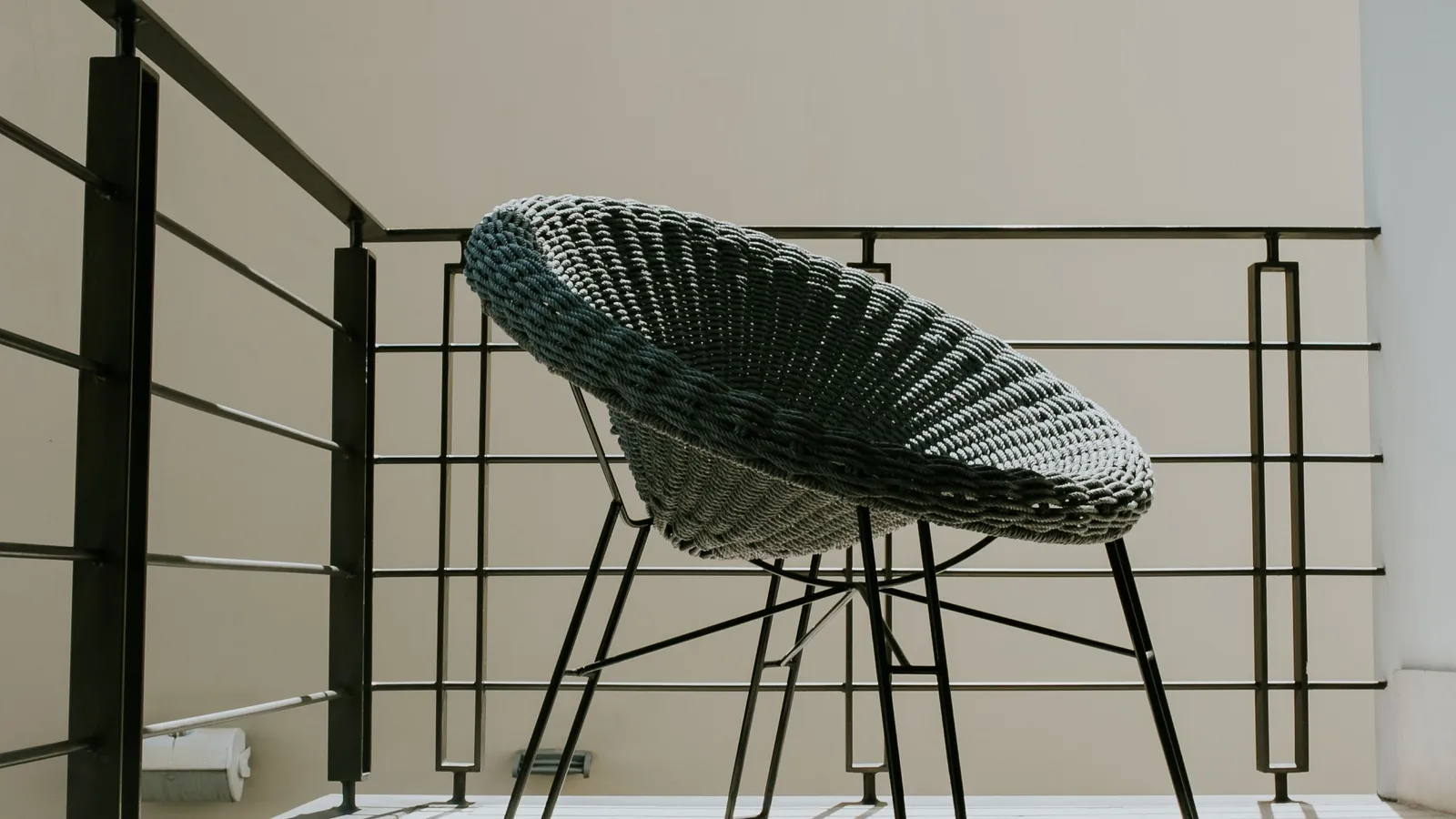 A woven scoop lounge chair on a minimalist apartment balcony in afternoon light