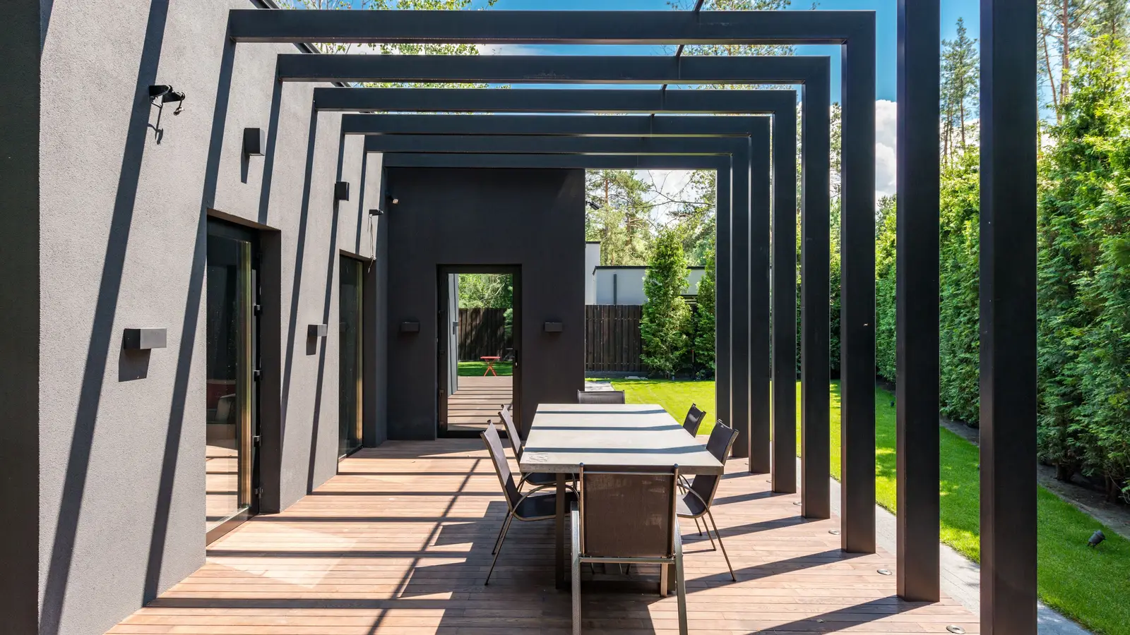 A modern black slatted pergola structure over an outdoor dining table