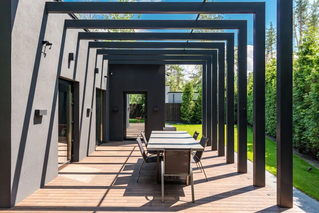 A modern black slatted pergola structure over an outdoor dining table