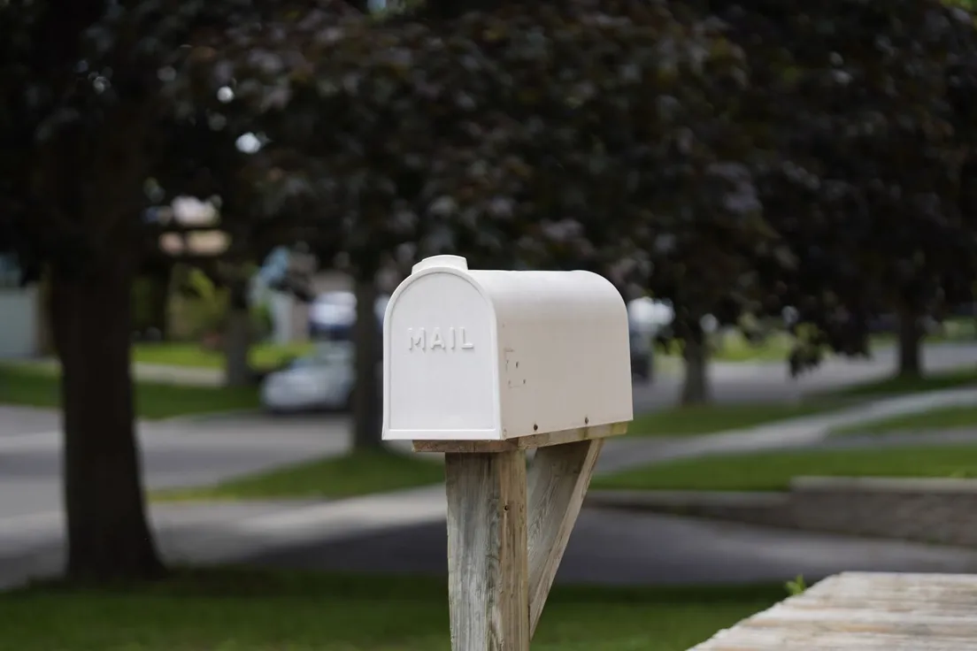 A classic white residential mailbox on a wooden post at the curb